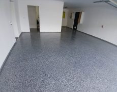 Große Garage mit weißen Wänden, graumelierten Garagenboden und 3 Durchgängen.