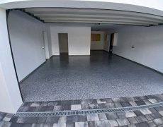 Große Garage mit weißen Wänden, graumelierten Garagenboden und 3 Durchgängen.