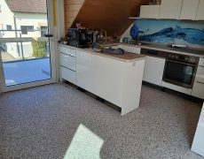 Offene Küche neben Terrassentür und mit hellgrauem Steinteppich.