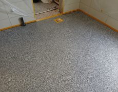 Graumelierter Boden in kleinem Raum mit Durchgang zu einer Küche.