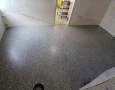 Graumelierter Boden in kleinem Raum mit Durchgang zu einer Küche.