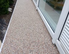 Terrasse erweitert entlang der Fensterfront mit braunmeliertem Boden.