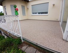 Terrasse mit hellbraunem Boden und weißem Geländer.