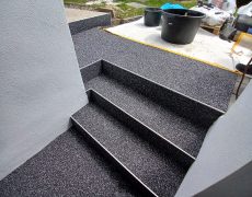 Treppe mit schwarzmeliertem Boden, die zum Garten führt, in dem Baumaterial steht.